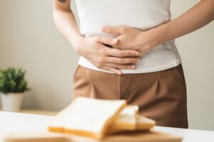 woman with celiac disease holding stomach next to slices of bread