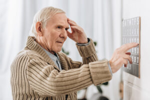 senior man pointing at calendar and touching his head