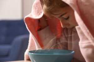 little girl breathing in steam over bowl of water